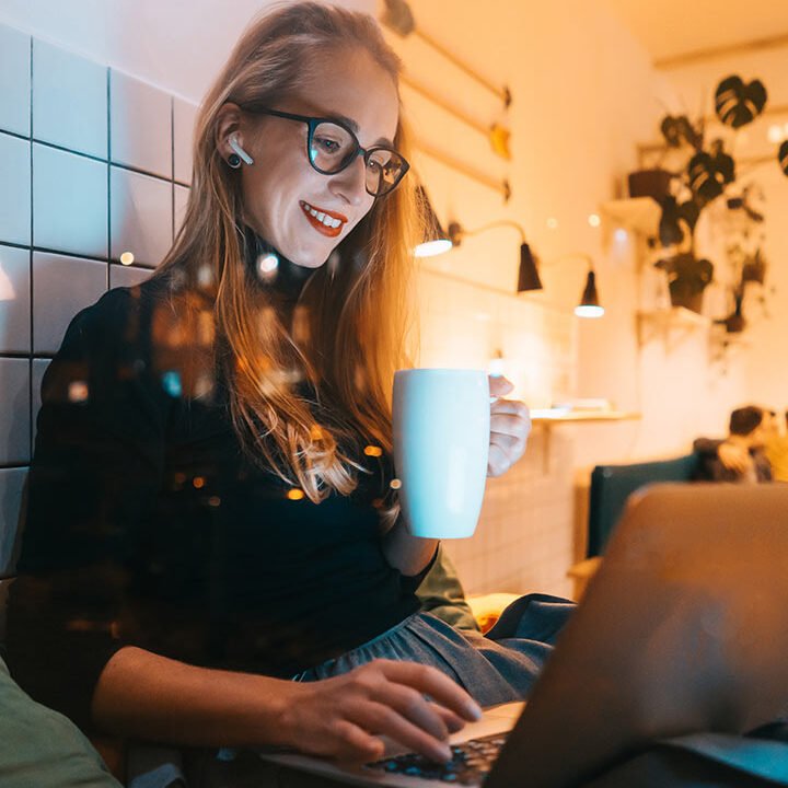 a woman sitting on a couch holding a cup of coffee and using a laptop